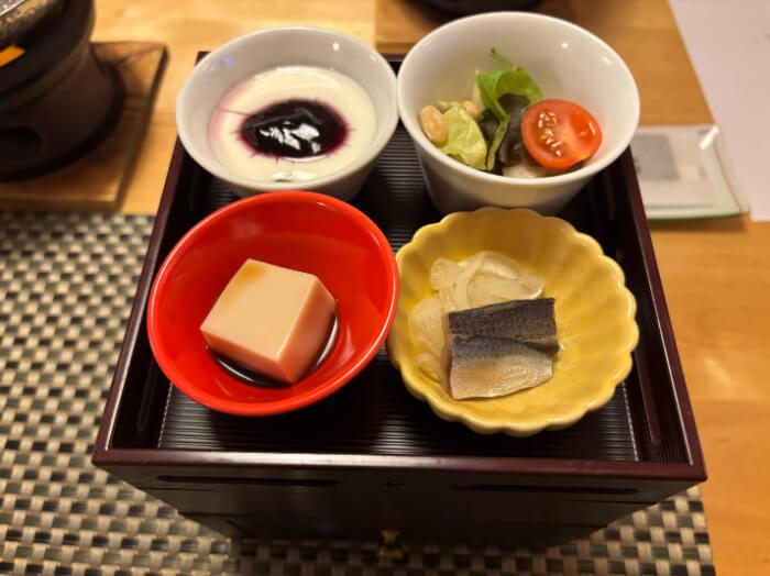 重箱と上段には小鉢に入ったサラダ、ブルーベリージャムがかかったヨーグルト、マリネ、ごま豆腐がある。