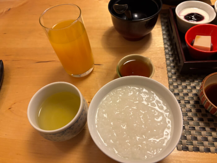 テーブルにのったオレンジジュース、緑茶、おかゆ、あん。