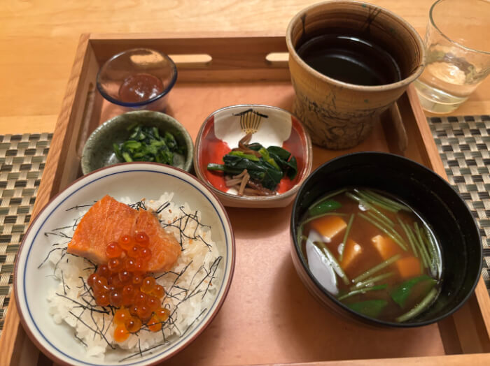 お盆の上に鮭いくらご飯、赤だしのみそ汁、つけもの、にんにく味噌、ほうじ茶がのっている。