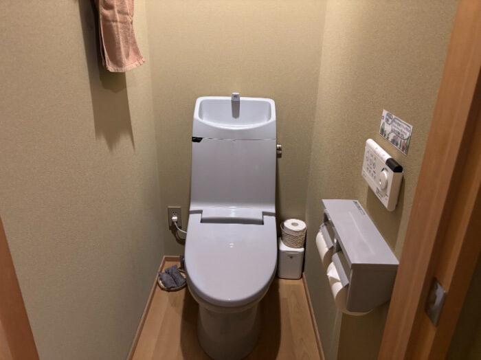 洋室ツインのウォシュレット付きトイレ。トイレットペーパーが2個と予備が1個。消臭剤の炭が置いてある。