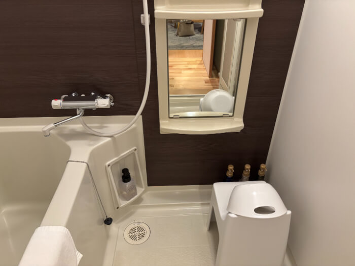 洋室ツインの浴室。備品は浴槽、桶、椅子、鏡、足拭きマット。アメニティはシャンプー、リンス、ボディソープがある。