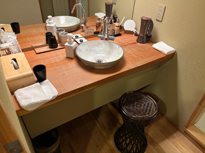 洗面台。腰掛け椅子が1つある。洗面ボールが1つ。お湯と水が出る。ドライヤー、手鏡、スキンケア、ハンドソープ、コップ2つ、ハンドタオル2つ、ティッシュペーパー、アメニティ各種がある。